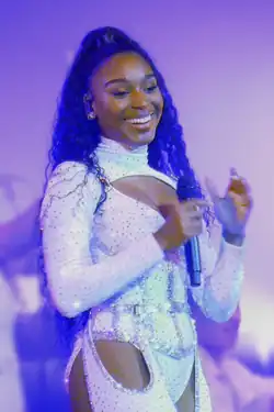 A young woman holds a microphone, looking right and smiling