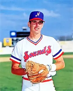 A man in a white baseball jersey and blue and red cap