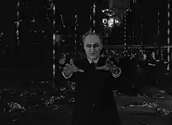 Pale man with dark shadows around his eyes, reaching forward