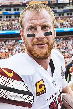 Man with red beard facing a camera and holding a football