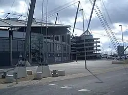 A grey stadium exterior with glass fronting. Adjoining it is a spiral walkway made of concrete, rising almost to the full height of the structure.