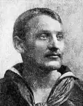 Head of a white man with mustache wearing a sailor suit with a wide flat collar open at the front.