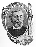 Head of a white man with a bushy goatee and thinning hair, wearing a dark suit coat and tie.