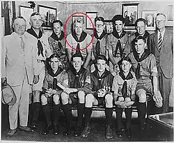 Two men in suits and another man in a boy scout uniform stand beside 10 seated teenaged boys in Boy Scout uniforms. Ford is indicated by a red circle.