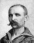 Head of a white man with a very wide handlebar mustache and closely cropped hair wearing a sailor suit.