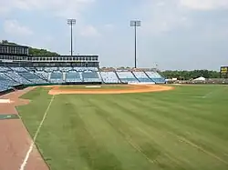 A view from the right-field line of the seating bowl at Greer. Blue seats stretch from the right-field wall, behind home plate, and beyond the third base dugout.
