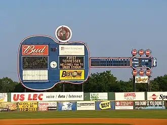 A view of the giant blue guitar-shaped scoreboard over the left-center field wall. There are advertisements for local businesses on the guitar and the green outfield wall below.