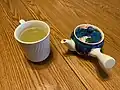 A white mug with gyokuro tea with a kyusu tea pot to the right of it