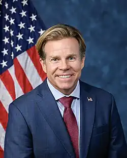 Official House portrait of Haridopolos smiling in front of the U.S. flag, wearing a dark blue suit with American flag lapel pin, light blue shirt, and red tie