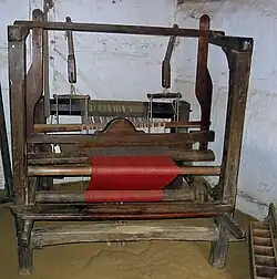 Hand loom at Hjerl Hede, Denmark, showing grayish warp threads (back) and cloth woven with red filling yarn (front)
