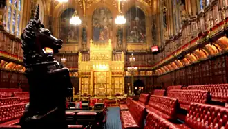 Wood panelled room with high ceiling containing comfortable red padded benches and large gold throne.