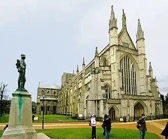 This exterior view at Winchester, taken from near the north west corner of the cathedral, and with a war memorial statue in the foreground, looks acutely along the north side of the building, showing it receding into the distance.
