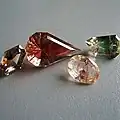 Four faceted gemstones in various cuts showing some of the Oregon labradorite colors, including dichroic red green, red and yellow bicolor, clear with copper shiller streaking, and teal blue-green.