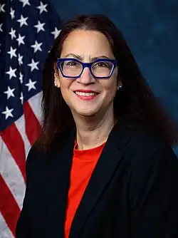 Official House portrait of Friedman smiling in front of the U.S. flag, wearing a black jacket and red shirt.