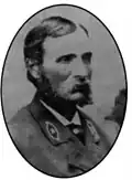 Head and shoulders of a white man with a mustache and long, bushy sideburns, wearing a suit coat with an oval emblem on each lapel.