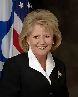 Woman with long brown hair with the US flag behind her