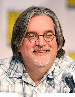 A man in glasses and a plaid shirt sits in front of a microphone.