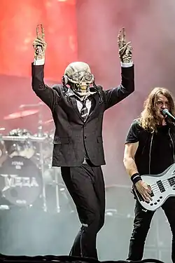 Vic Rattlehead posing at a concert. He is a skeleton in a business suit.