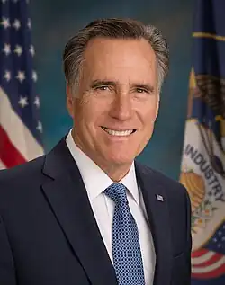 Dark-haired man with graying hair at the temples, dressed in dark suit, at a nighttime indoor