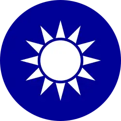 A blue circular emblem on which sits a white sun composed of a circle surrounded by 12 rays.