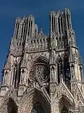 The West Front or facade of Reims, showing two towers, three portals with sculptured figures, and a rose window.