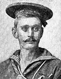 Head of a white man with handlebar mustache wearing a sailor suit and a flat cap.