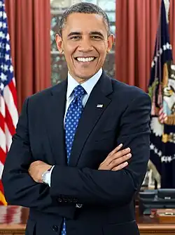Obama standing in the Oval Office with his arms folded and smiling