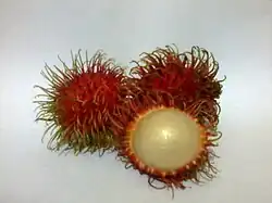 two unpeeled fruits with red spiky skin and one peeled fruit with white inside