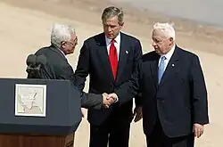 Palestinian Prime Minister Mahmoud Abbas and Israeli Prime Minister Ariel Sharon shaking hands. President of the United States George W. Bush stands in the middle.