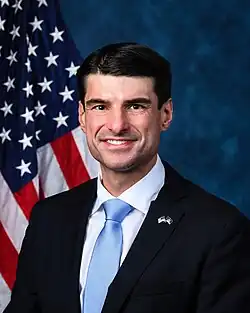 Official House portrait of Bresnahan smiling in front of the U.S. flag, wearing a black suit with American and Pennsylvanian flags lapel pin, white shirt, and blue tie.