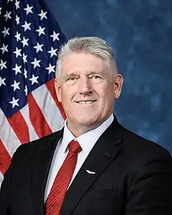Official House portrait of Downing smiling in front of the U.S. flag, wearing a black suit with an Army Aviator Badge, white shirt, and striped red tie.