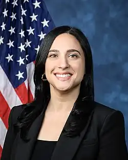 Official House portrait of Ansari smiling in front of the U.S. flag, wearing a black shirt.