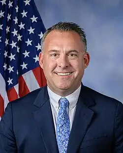 Official House portrait of Gray smiling in front of the U.S. flag, wearing a black suit, white shirt, and blue floral tie.
