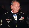 A gray-haired white man wearing a formal military uniform with a star-shaped medal hanging from a ribbon around his neck