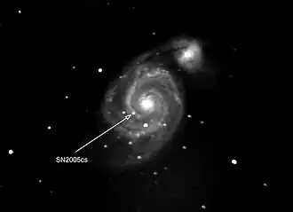 Photograph of supernova in another galaxy. The supernova is pointed by the arrow. The other bright spots are stars of our own galaxy that happen to be in front of the other galaxy