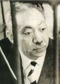 A photo shows Sayyid Qutb behind jail bars. He is wearing a Western style suit and striped tie. It is the only known photo of him on trial before his execution.