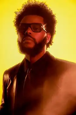 Tesfaye (the Weeknd), wearing a black suit with a bowtie, and with a neutral expression on his face, averts his gaze from the camera.