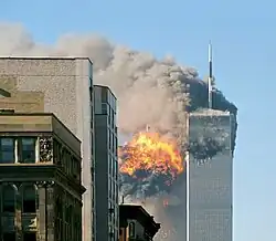 Two tall, gray, rectangular buildings spewing black smoke and flames, particularly from the left of the two.