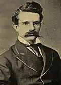 Head and shoulders of an older white man with a bushy beard wearing a suit coat, vest, and bow tie.