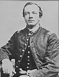 Head and torso of a white man with a tuft of hair on his chin, wearing a military jacket buttoned only at the neck.