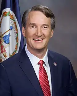 Head shot of Youngkin smiling in front of the flag of Virginia